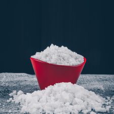 Sea salt in a red bowl and around on a dark textured and black background. side view. Sea salt in a red bowl and around on a dark textured and black background. side view.